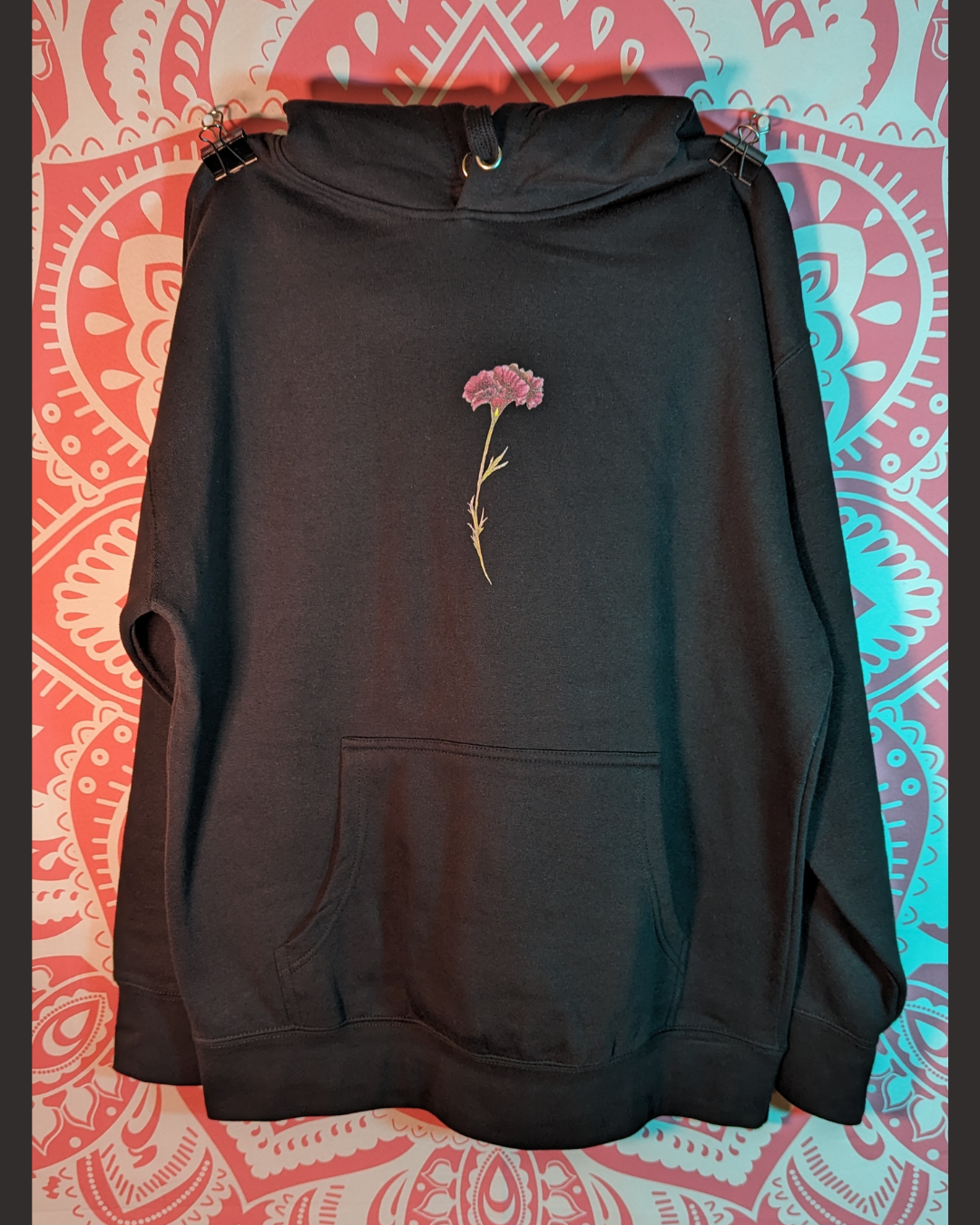 Pink and green carnation flower on front of black unisex print on demand Only Love. hoodie with original artwork from Amy-Lynn Denham